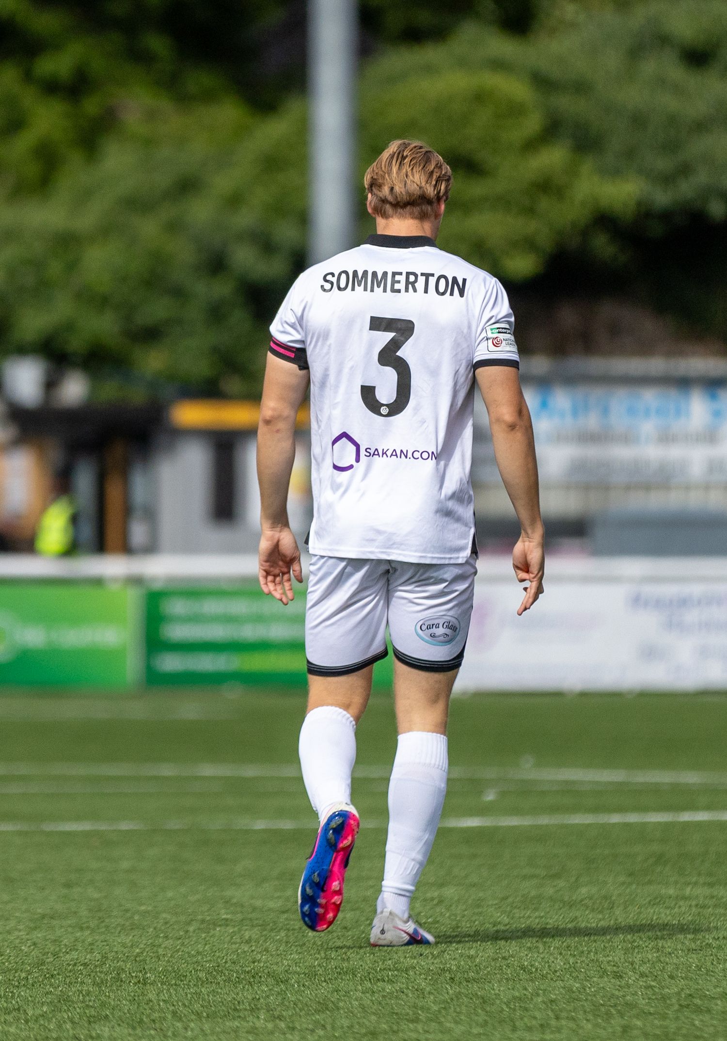 Soccer player Sommerton wearing number 3 white jersey walks on green field during sunny match day.