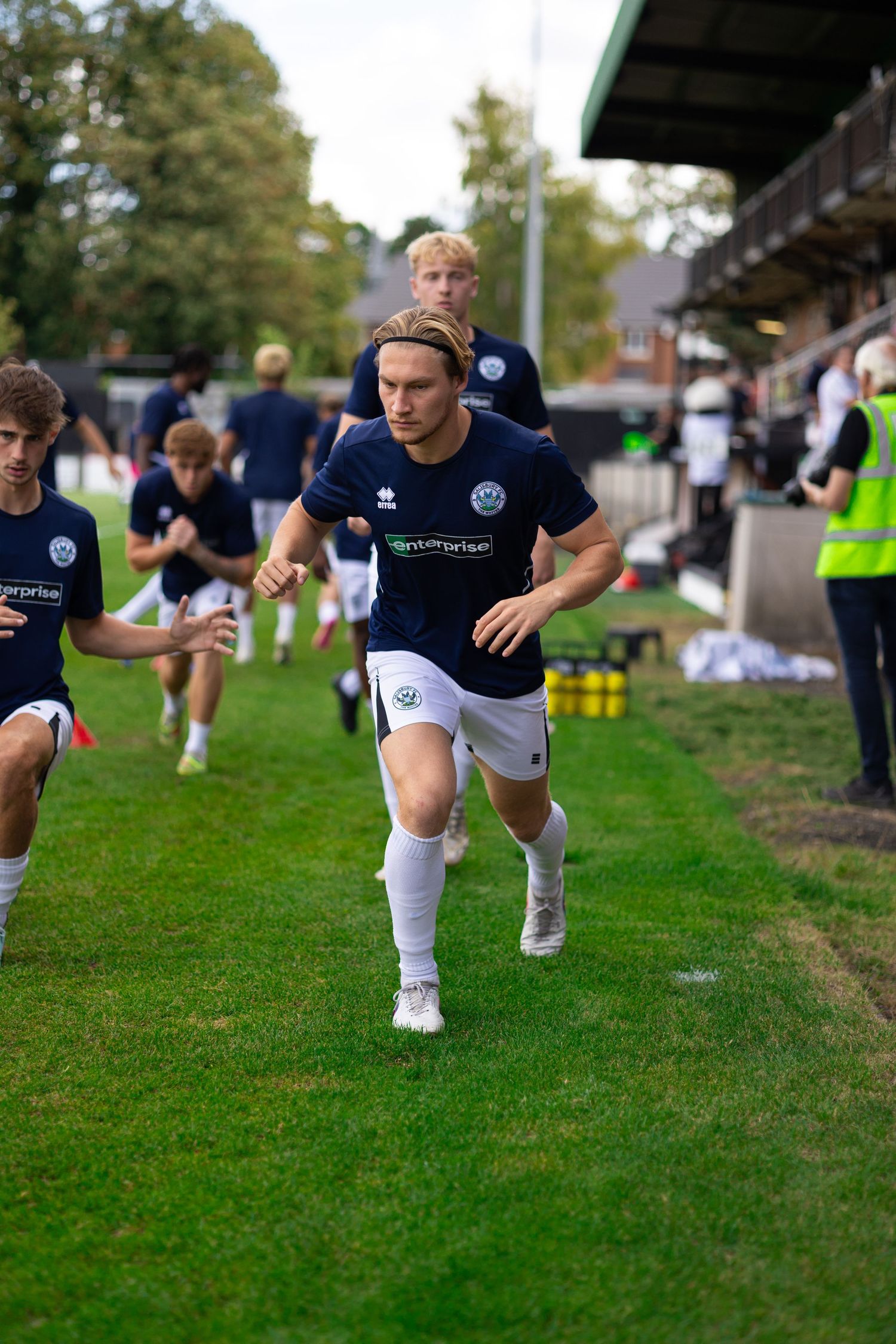 Soccer players in navy uniforms warming up on a green pitch before a match at an outdoor stadium.