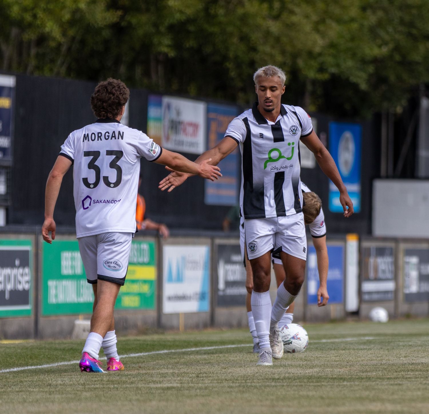 Soccer player number 33 Morgan high-fives teammate during a football match in black and white striped kit.