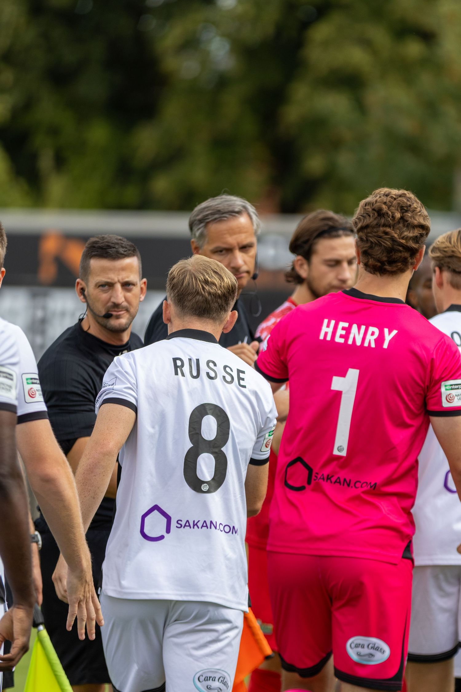 Players in black and white and pink kits shake hands with referees before a match.