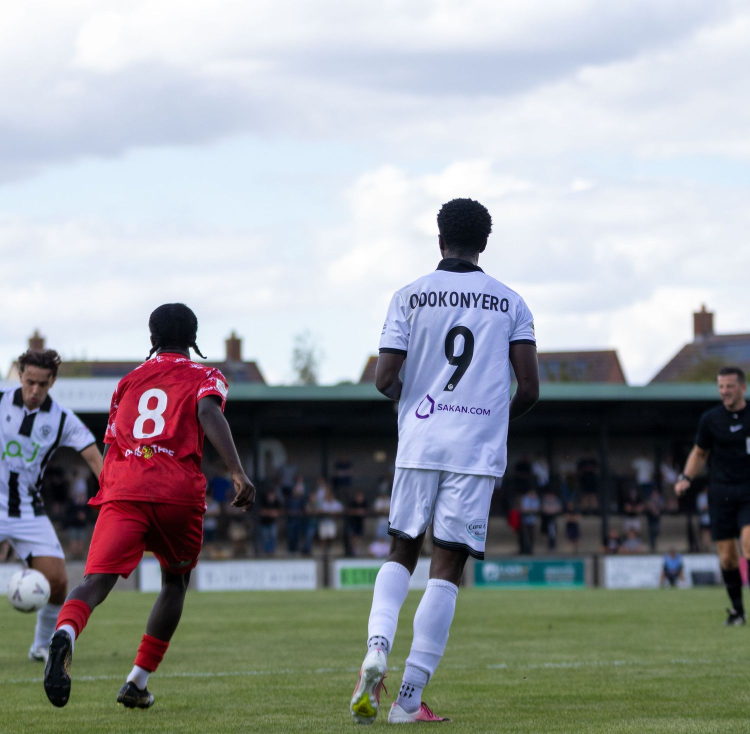 Player number 9 Ojokonyero in white kit controls ball during a non-league football match on a sunny day.