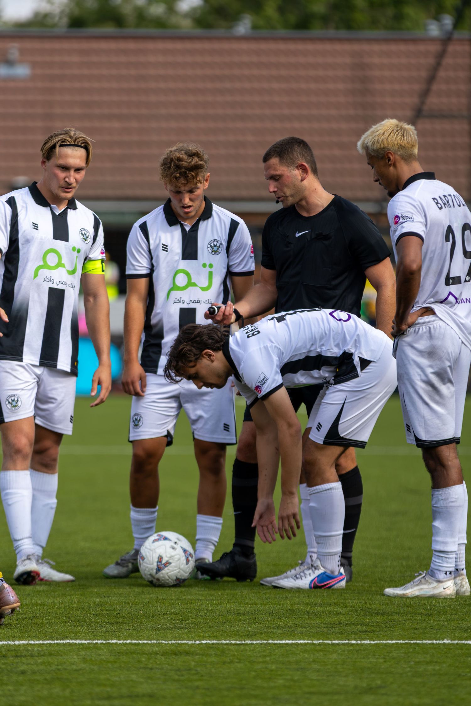 Referee places ball on pitch surrounded by white kit players including Bartoli number 29.