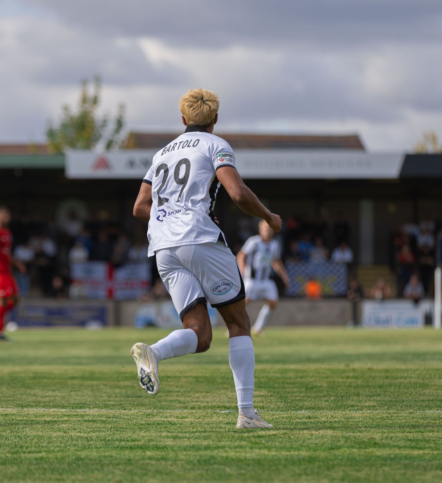 Soccer player number 29 Bartolo running on green field during outdoor match with spectator stands in background.