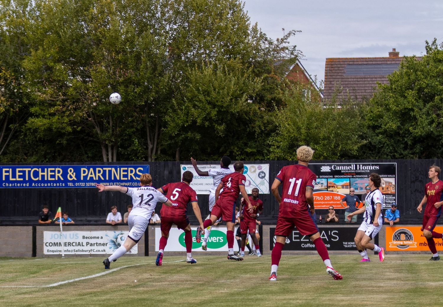 Salisbury FC player number 12 attempts a shot during an outdoor football match on a sunny day.