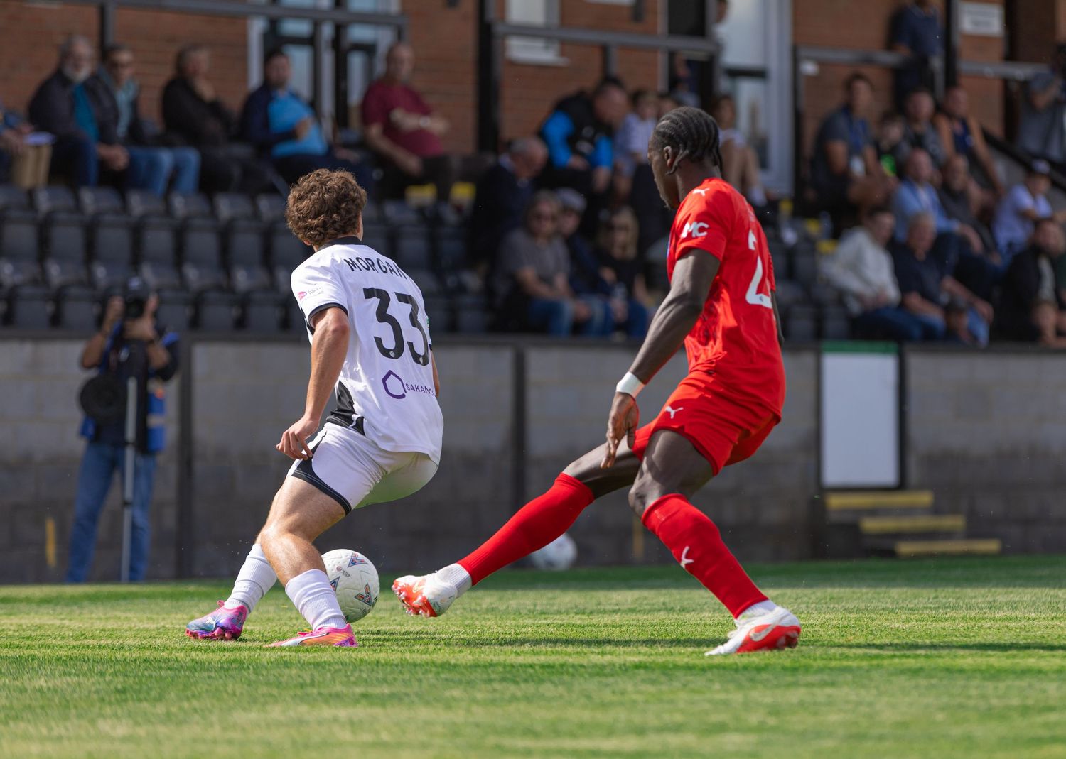 Two soccer players compete for the ball during a match, one wearing red and another in white number 33 jersey.
