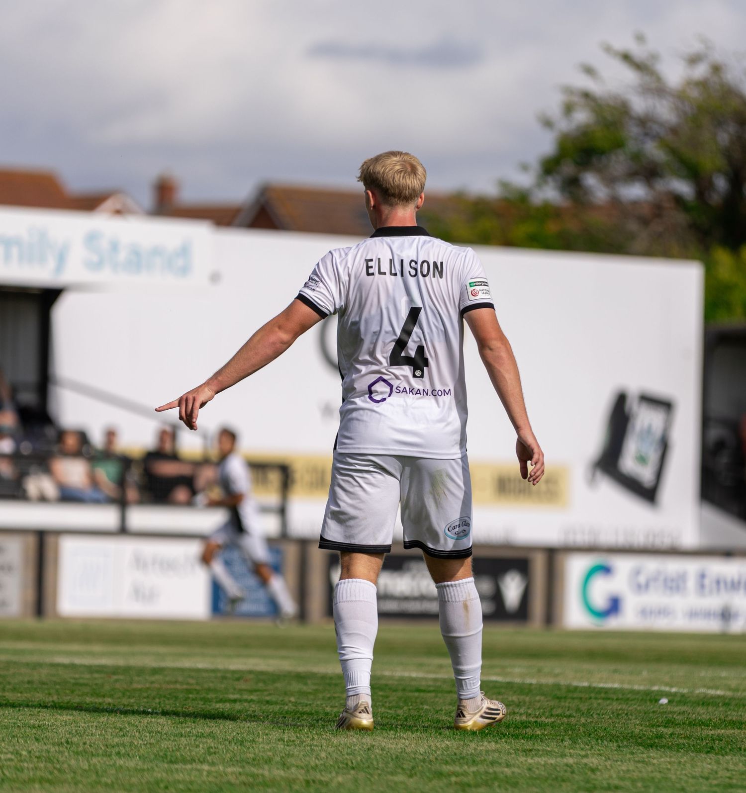Football player Ellison wearing number 4 white kit stands on green pitch during a sunny match day.