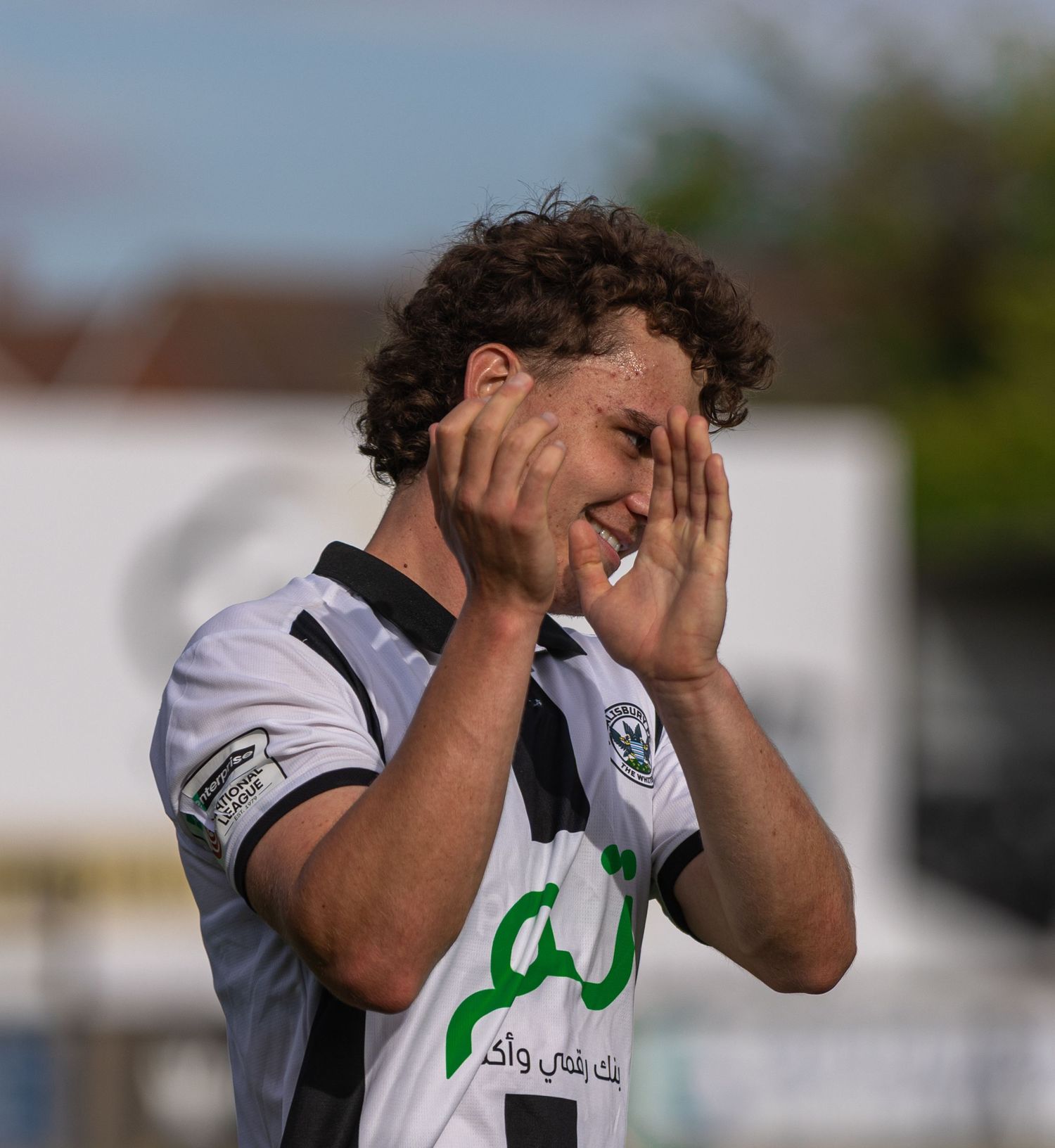 A young soccer player in a white jersey covers his face with both hands during a match outdoors.