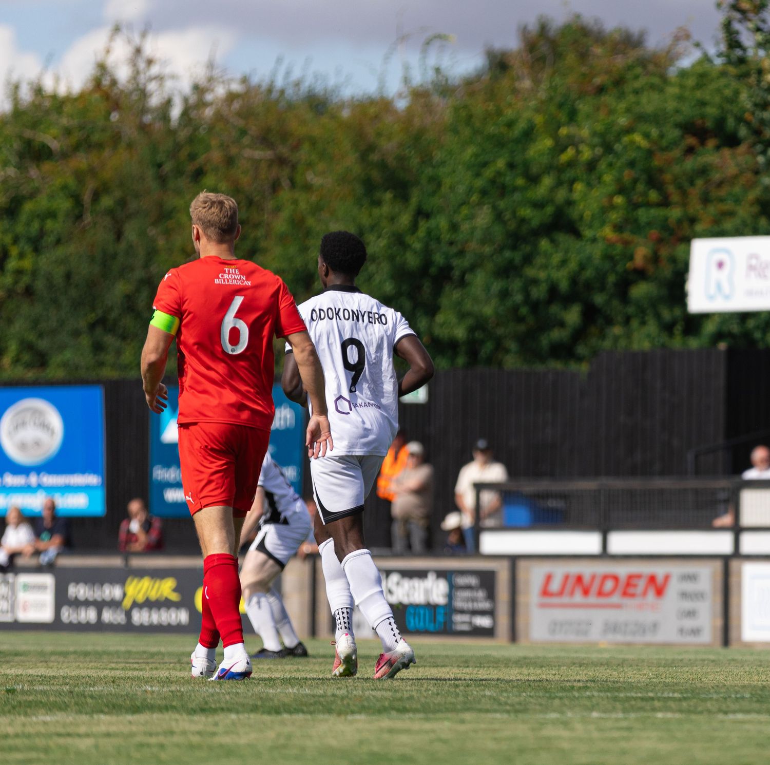 Two soccer players, wearing red number 6 and white number 9 jerseys, walk on a sunny outdoor pitch during a match.