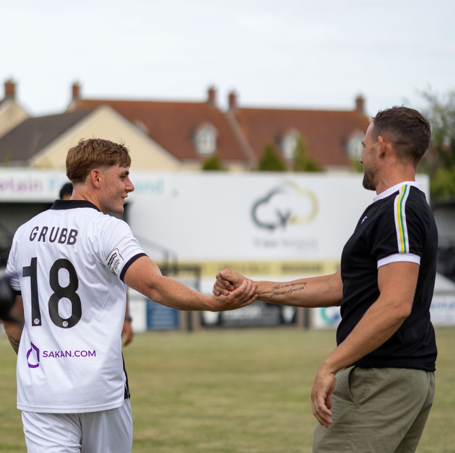 Footballer GRUBB number 18 in white SAKN.COM jersey fist bumps a coach on the sideline.