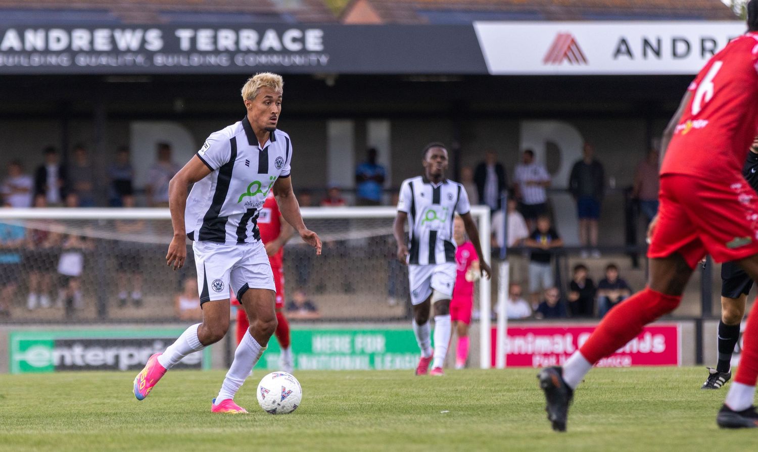 A footballer in black and white kit dribbles the ball during a non-league match at Andrews Terrace ground.