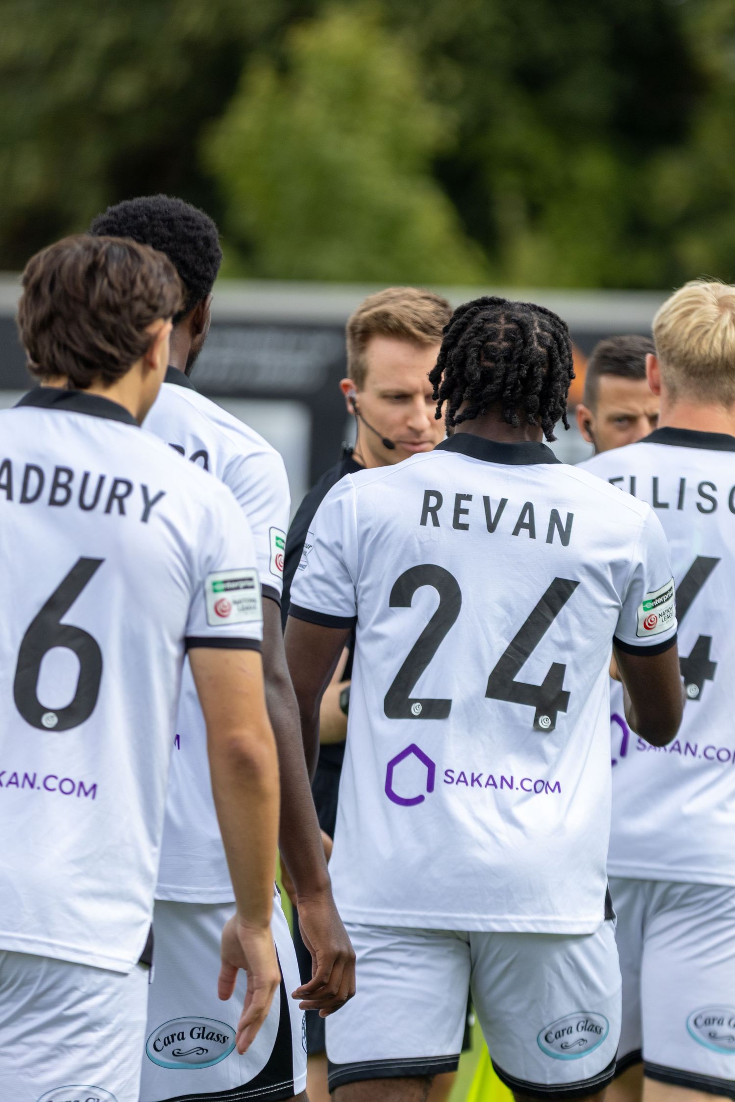 Footballers Bradbury, Revan number 24 and Ellison in white Sakan.com sponsored kits huddle.