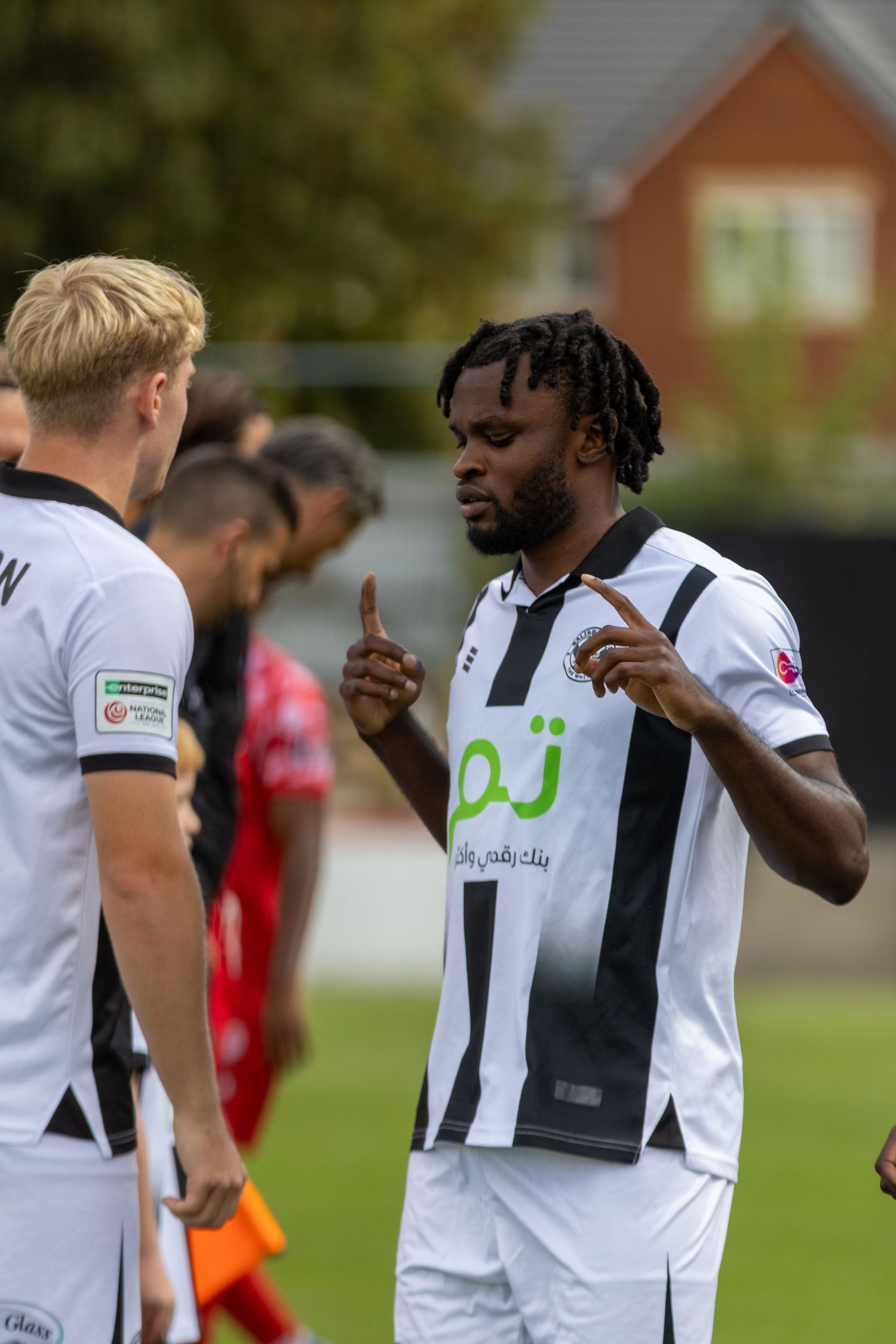 A footballer in black and white stripes gestures with raised fingers during a match.