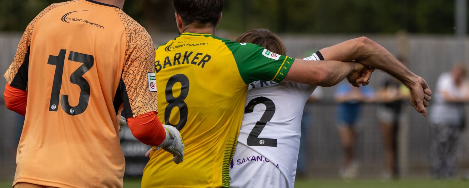 Soccer players in green and yellow jerseys compete during a match, with player Barker number 8 visible.