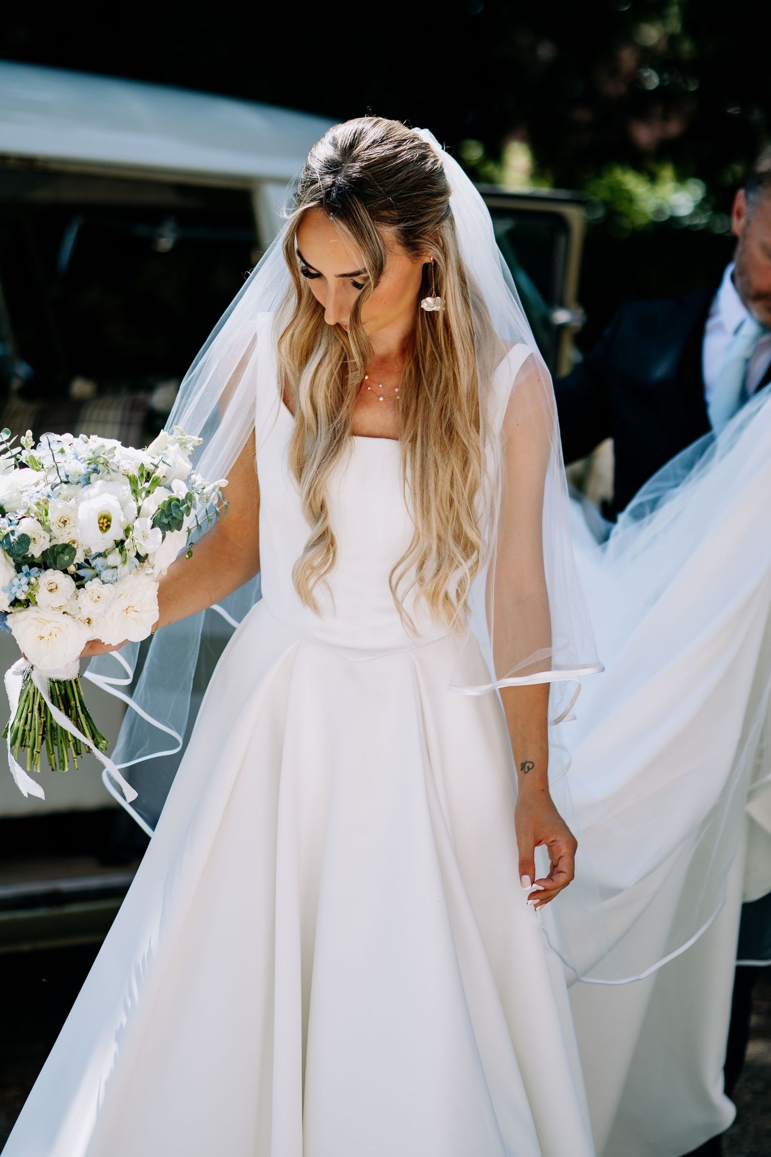 Beautiful blonde bride wearing white wedding dress and veil carrying white and green bouquet.