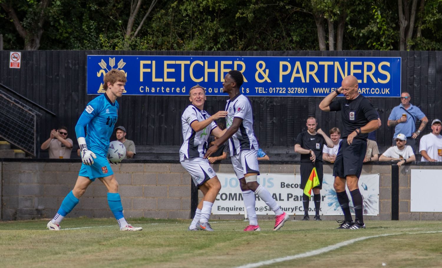 Salisbury FC players celebrate a goal in front of the Fletcher & Partners advertisement board during a match.