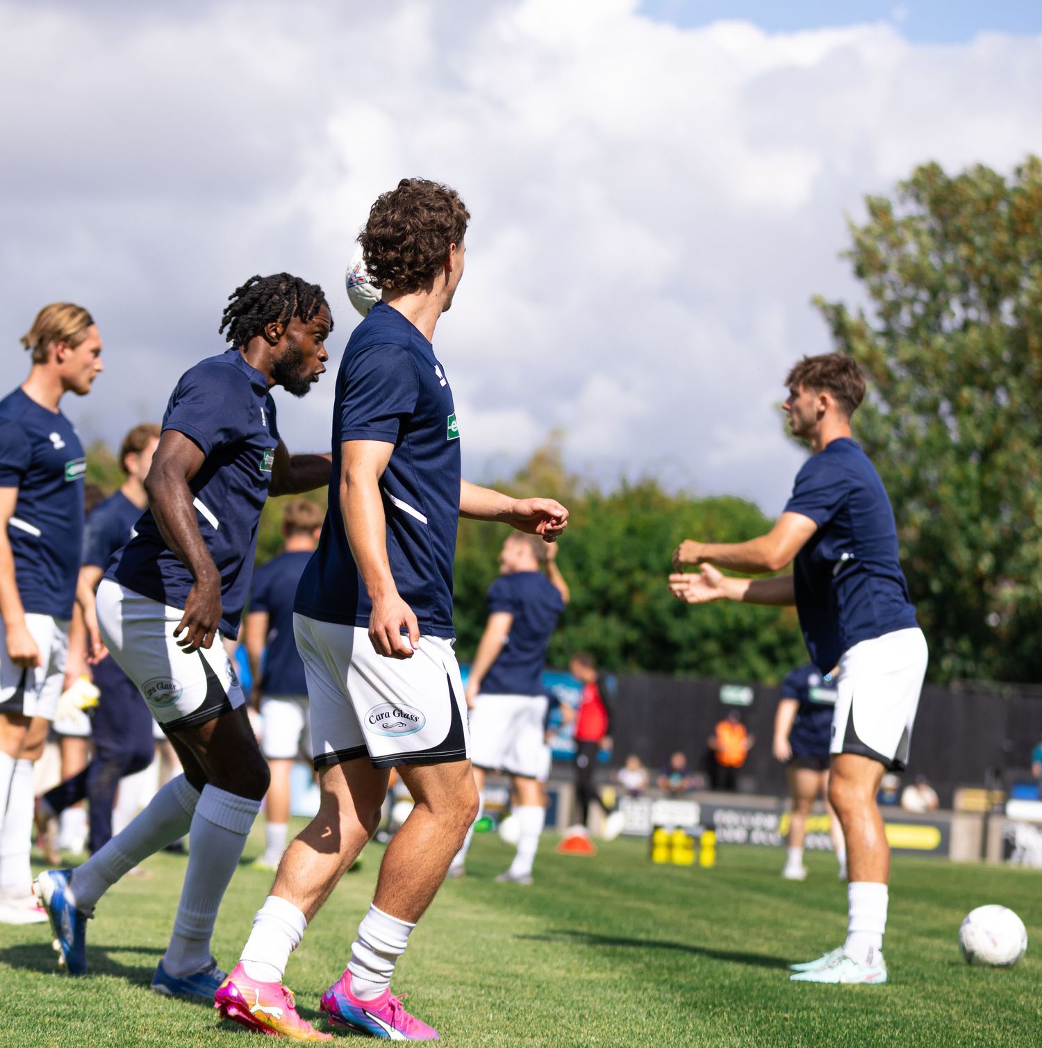Soccer players in navy uniforms training on a green field during an outdoor practice session on a cloudy day.