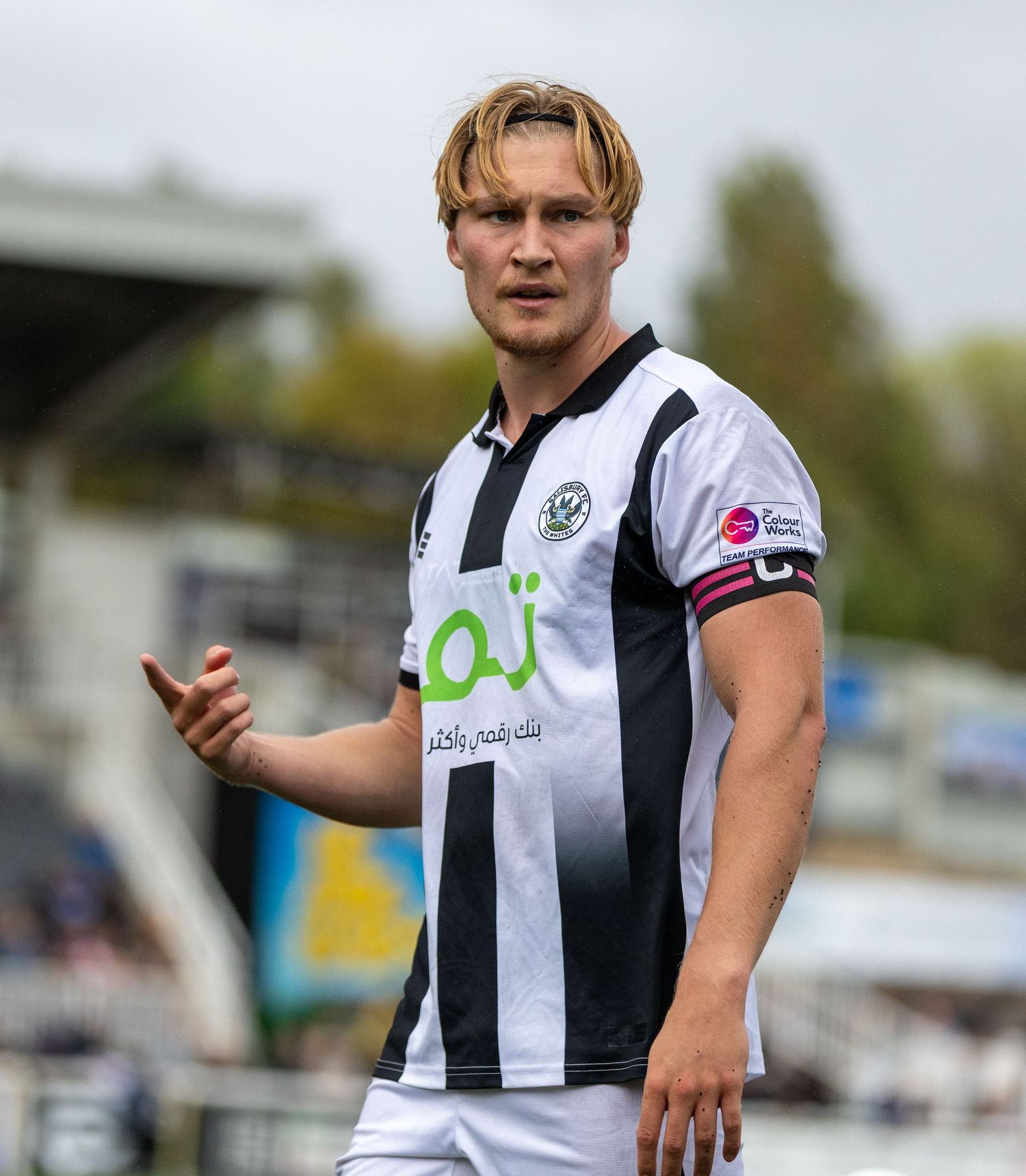 A young male soccer player in a black and white striped jersey gestures on the field during a match.