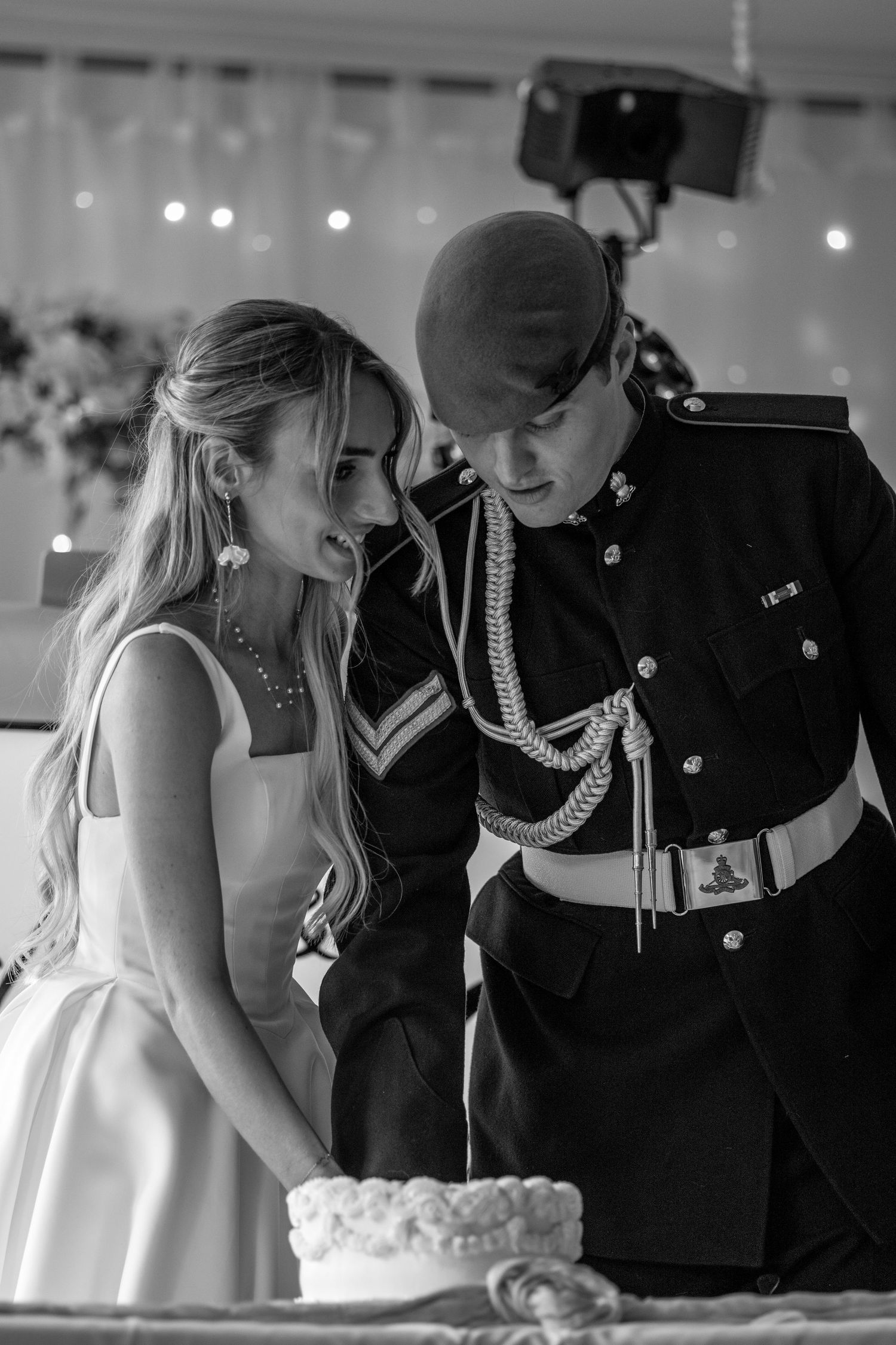 Black and white photo of bride and military groom cutting wedding cake at reception.