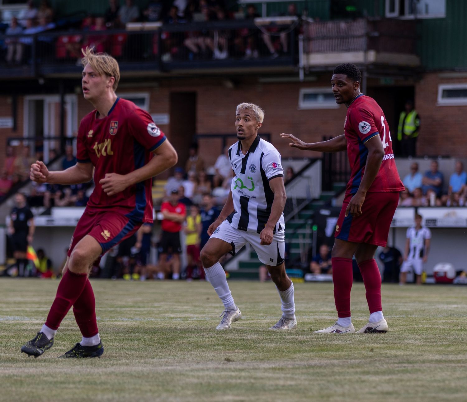 Football players in claret and white kits compete during an outdoor match on a well-maintained grass pitch.
