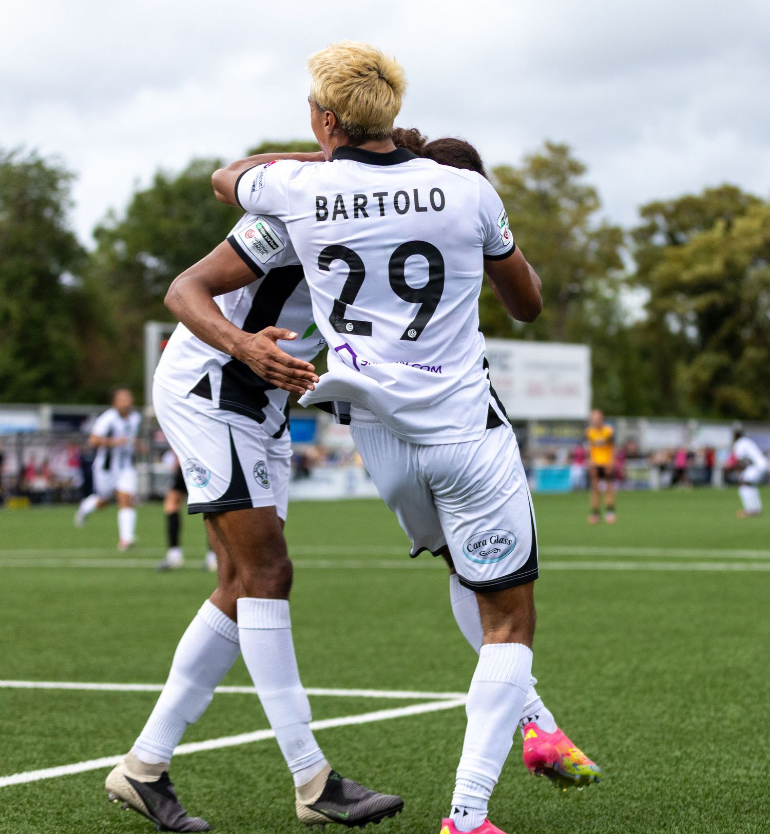 Soccer player Bartolo wearing number 29 celebrates a goal with a teammate on a green field.