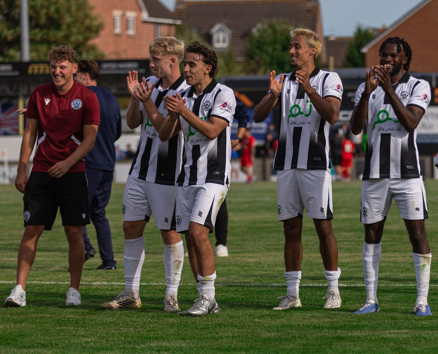 Football players in black and white striped kits applauding fans after a match on a sunny day.