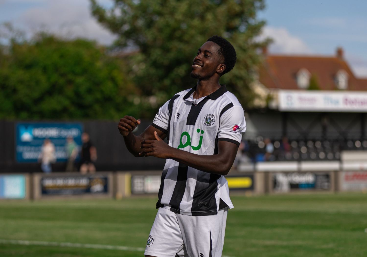 A joyful footballer in black and white kit celebrates on a sunny pitch during a match.
