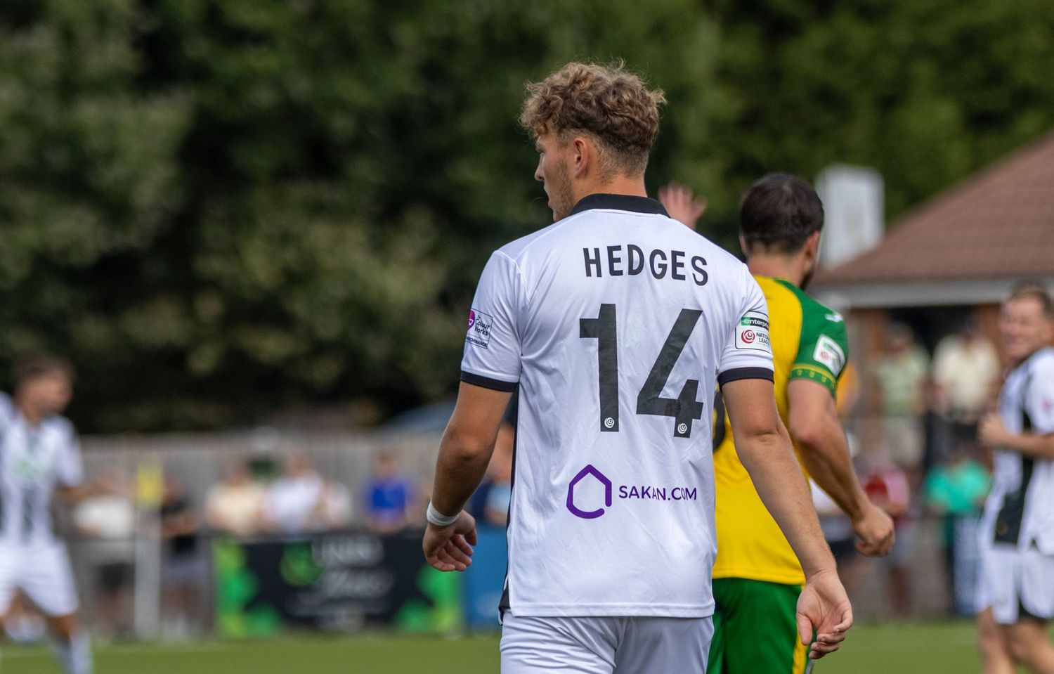 Soccer player Hedges wearing number 14 white jersey walks on green pitch during a sunny match.