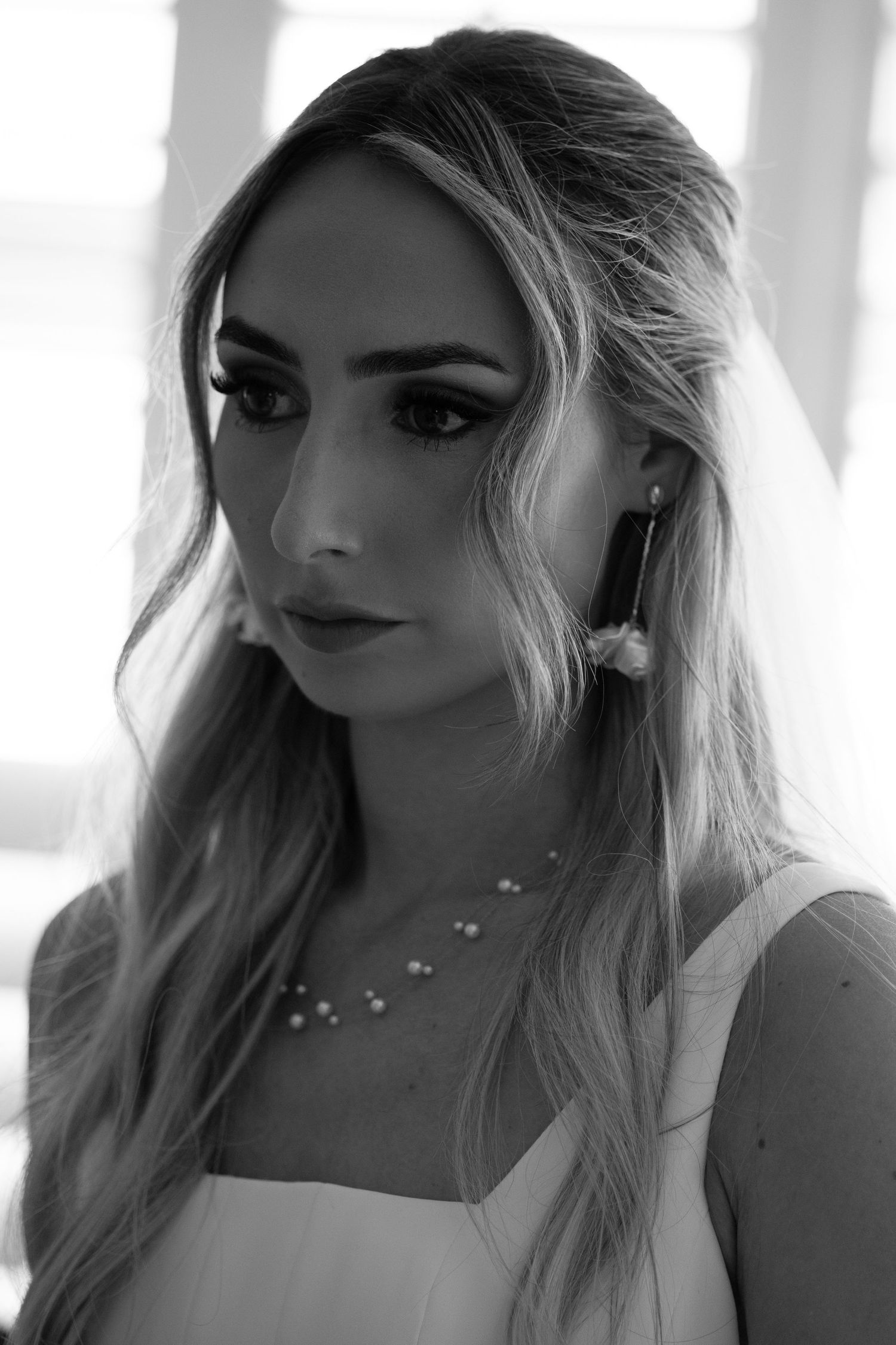 Elegant bride in black and white portrait wearing pearl necklace and drop earrings with veil.