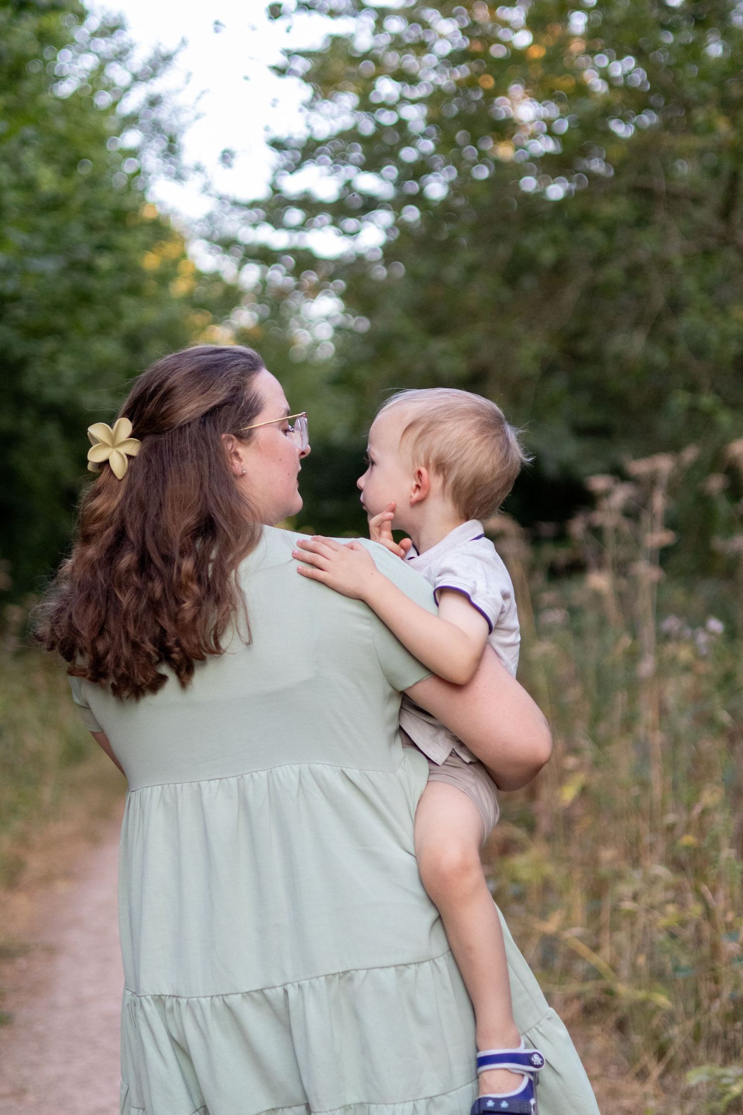 A mother holding her happy toddler on a lush green nature path, both sharing a joyful moment.