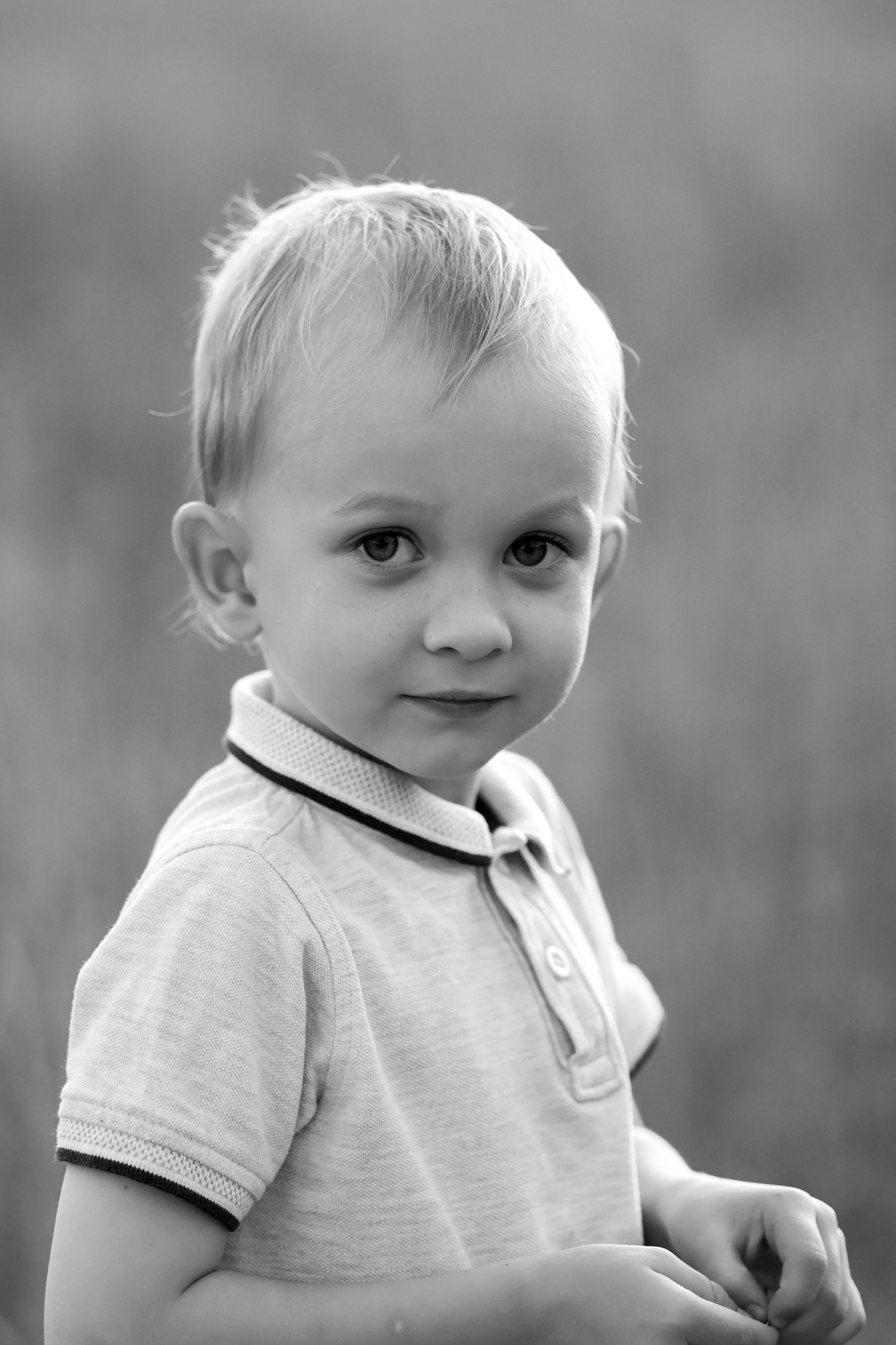 Black and white portrait of a young blonde toddler boy in a polo shirt outdoors.