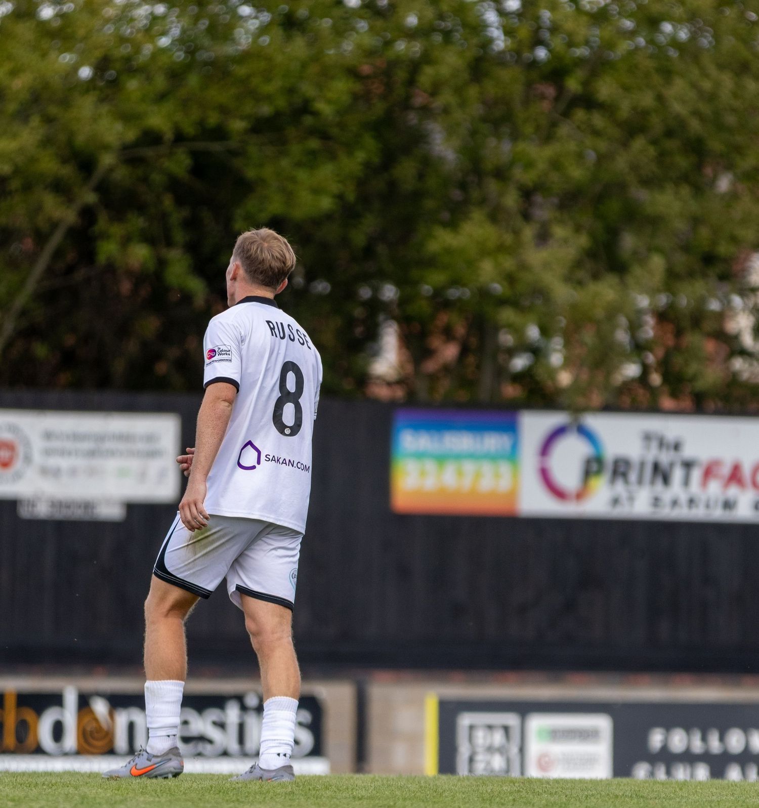 Soccer player wearing number 8 white jersey walks on field near advertising boards during a match.