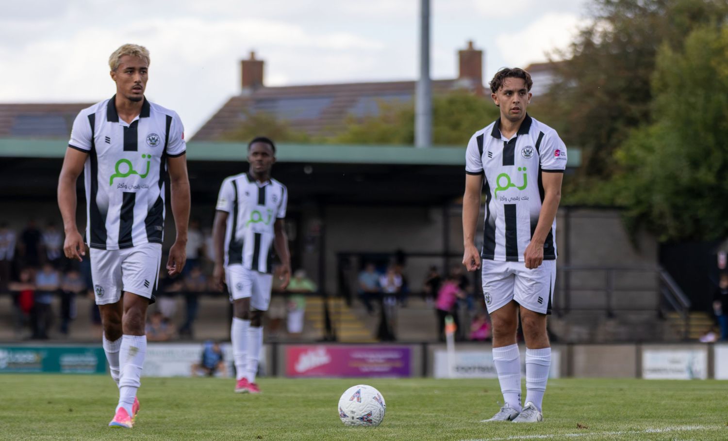 Two footballers in black and white kits line up beside a ball on a green pitch.