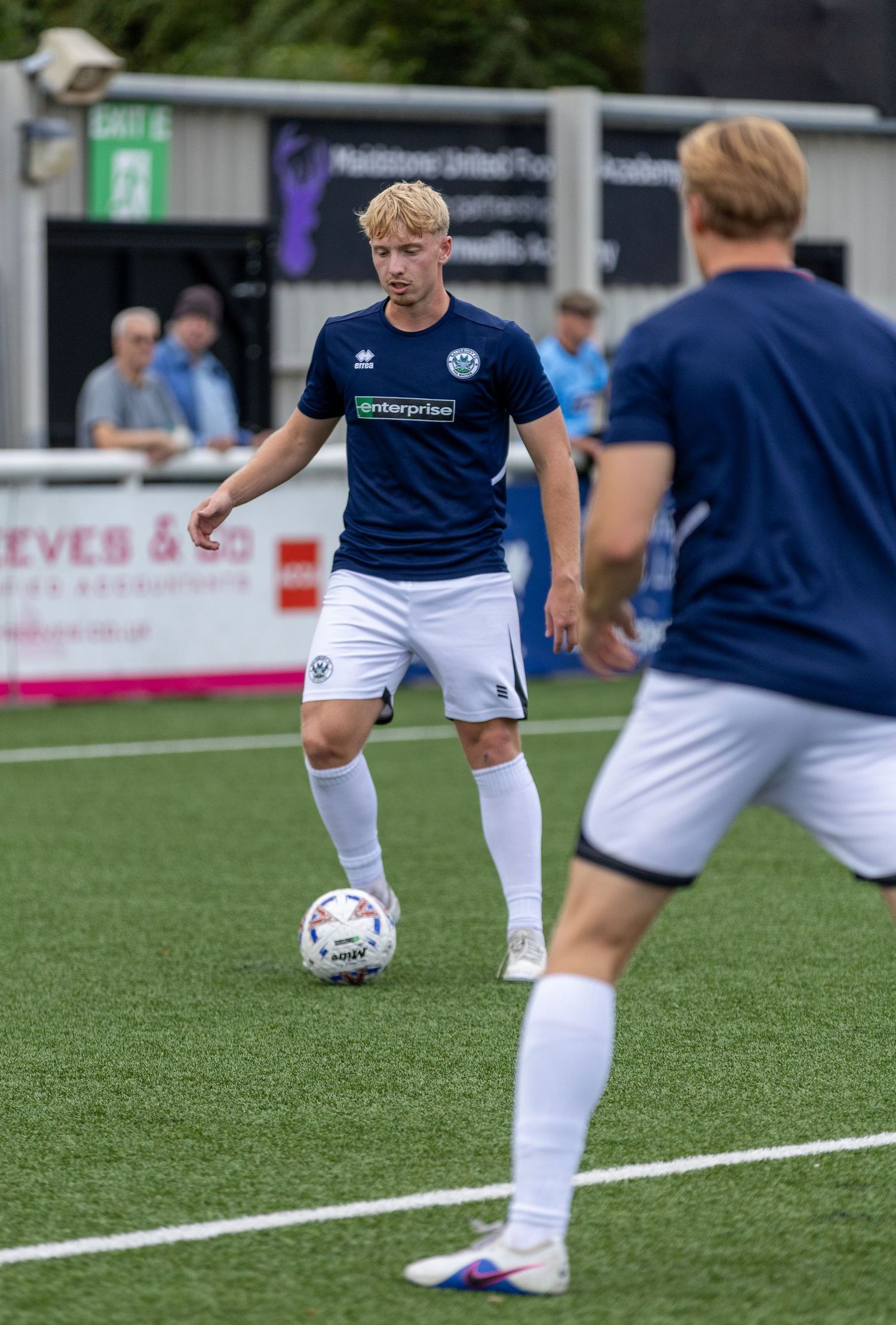Young footballer in navy Enterprise kit controls the ball during a match at Maidstone United Football Academy.