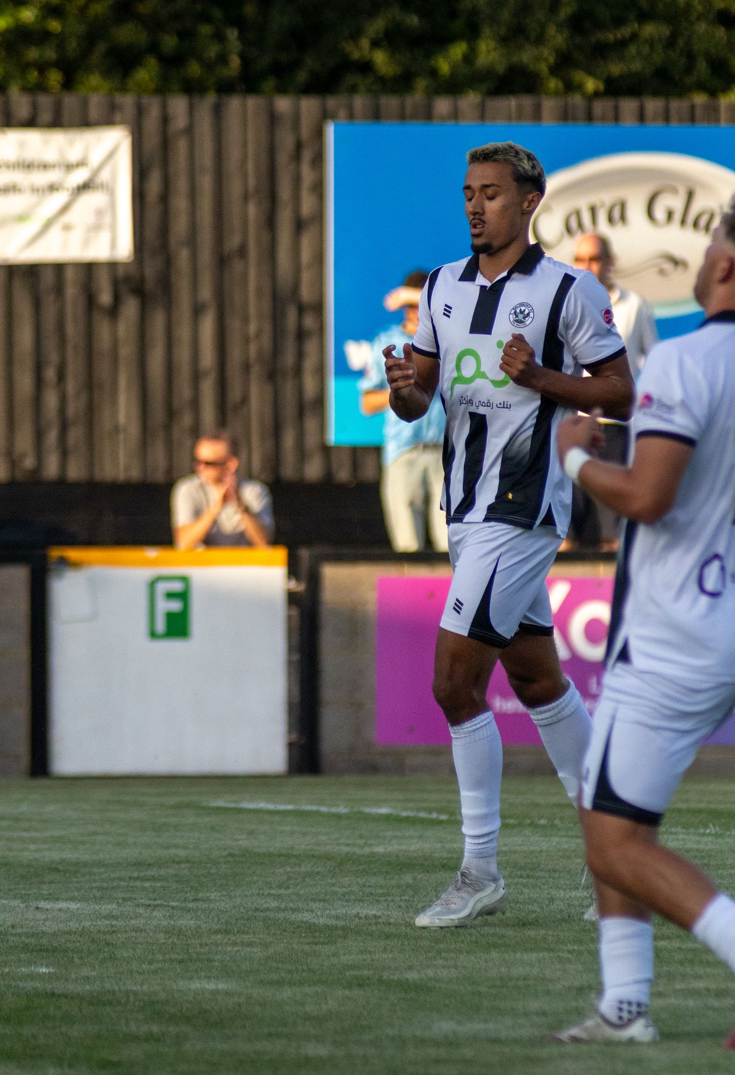 A soccer player in white and dark blue kit runs during a match at an outdoor football ground.