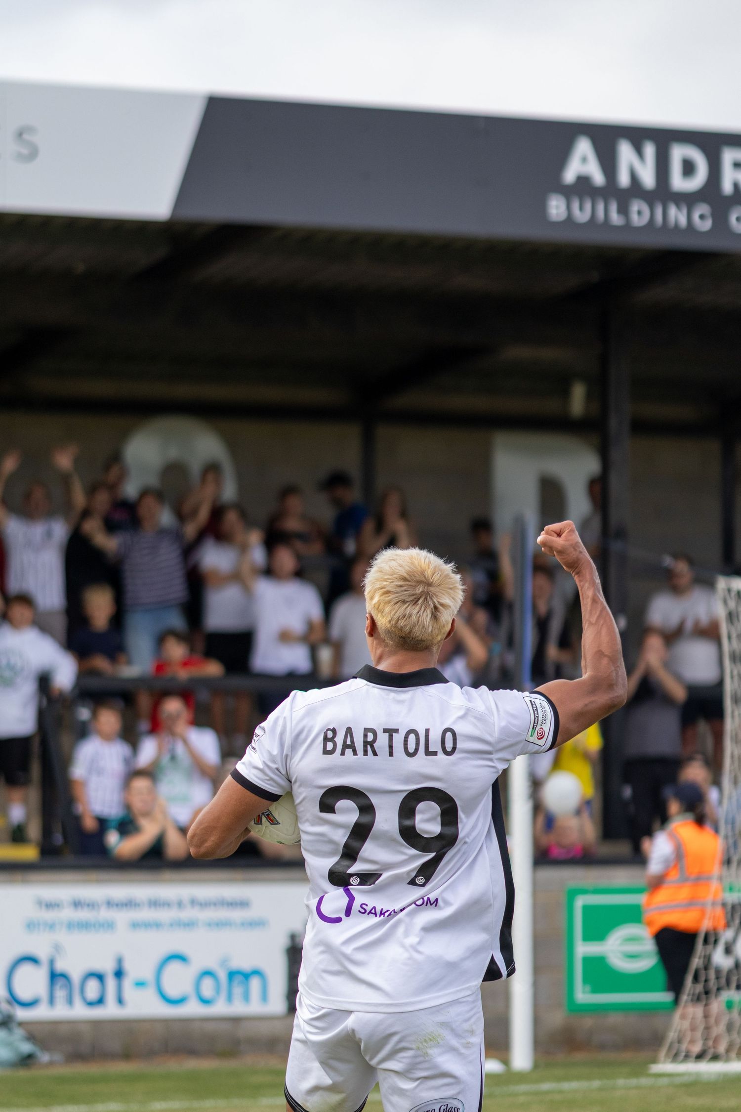 Bartolo number 29 in white kit raises fist celebrating goal with cheering crowd at stadium.