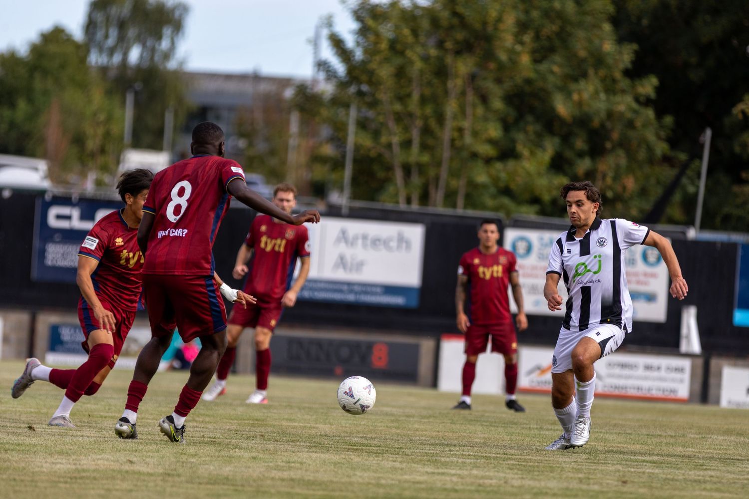 A soccer player in black and white dribbles past opponents in maroon during an outdoor match.