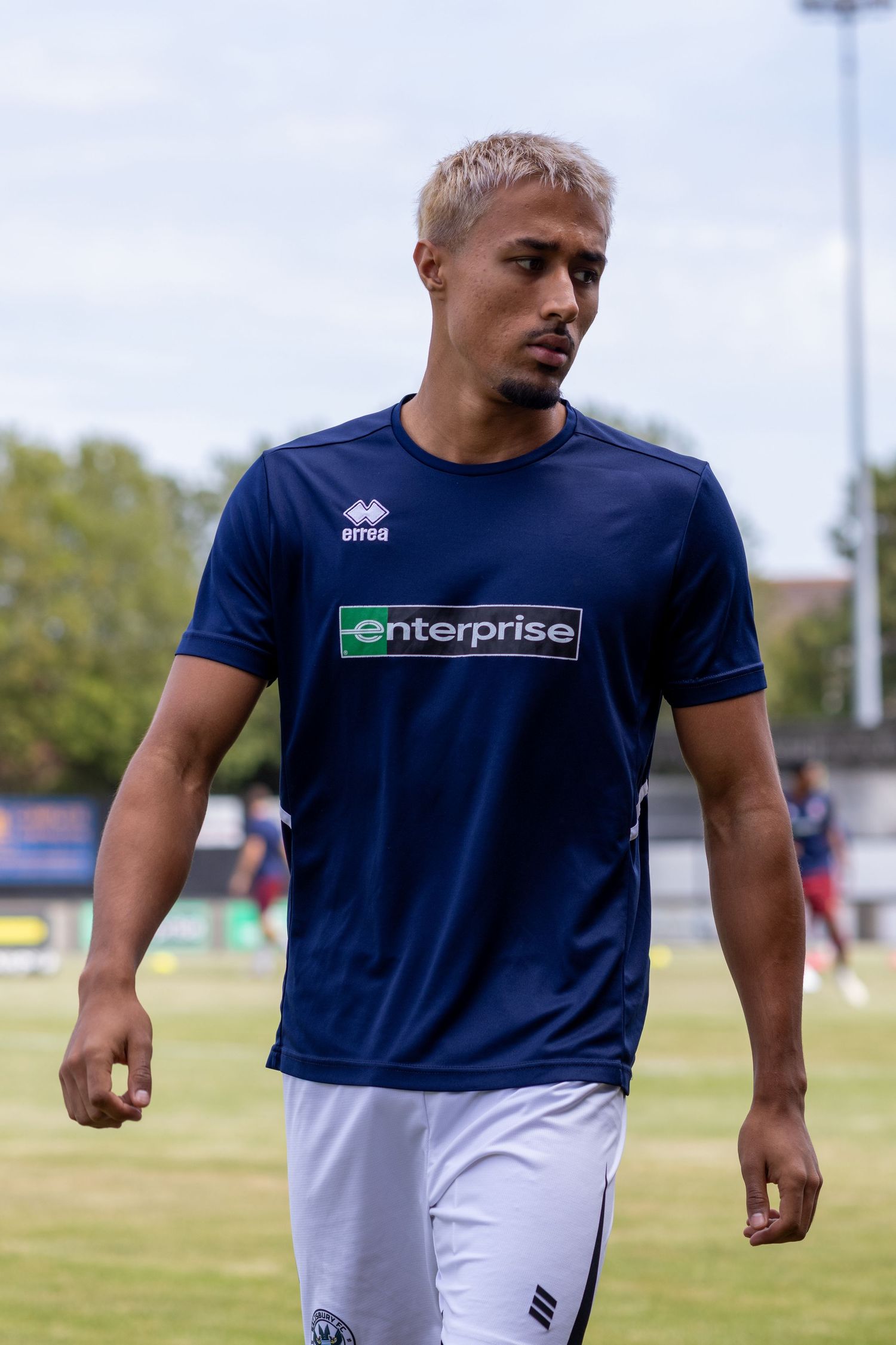 Mixed-race footballer with blonde hair in navy Enterprise Errea shirt during pre-match warmup.