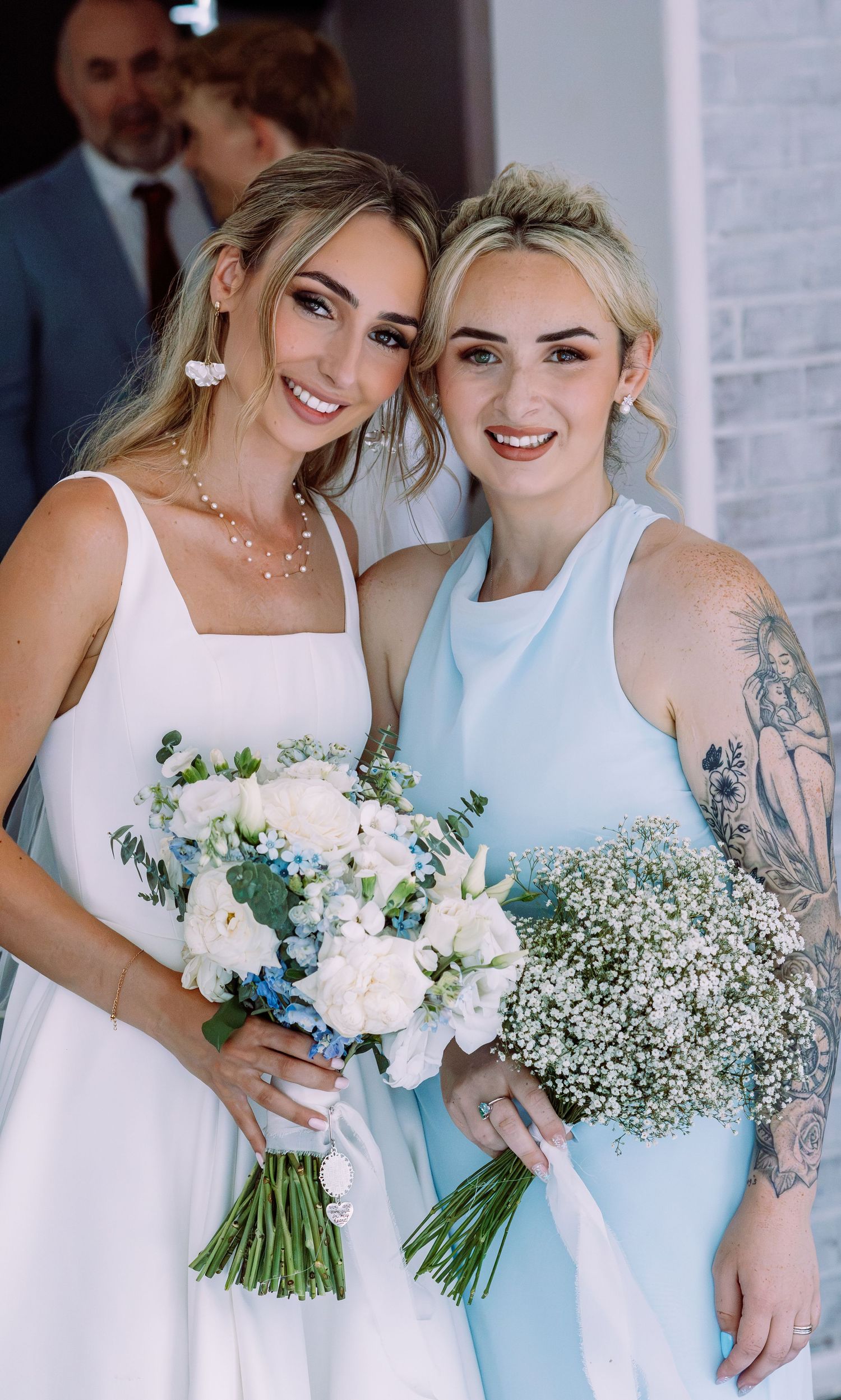 Bride in white dress and bridesmaid in light blue holding floral bouquets at a wedding ceremony.