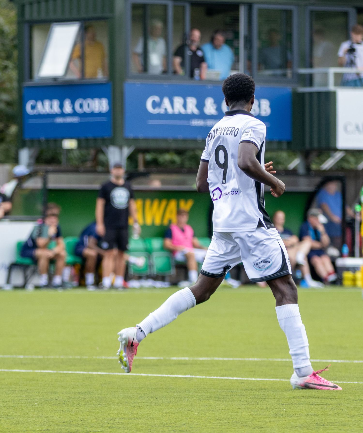 Footballer number 9 Okonyero in white kit runs on the pitch with Carr and Cobb signage behind.