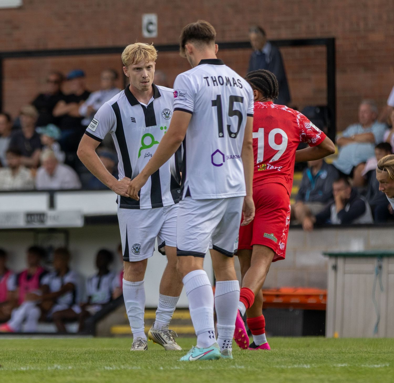 Two soccer players in white uniforms, number 15 Thomas, stand on field near opponent in red during a match.