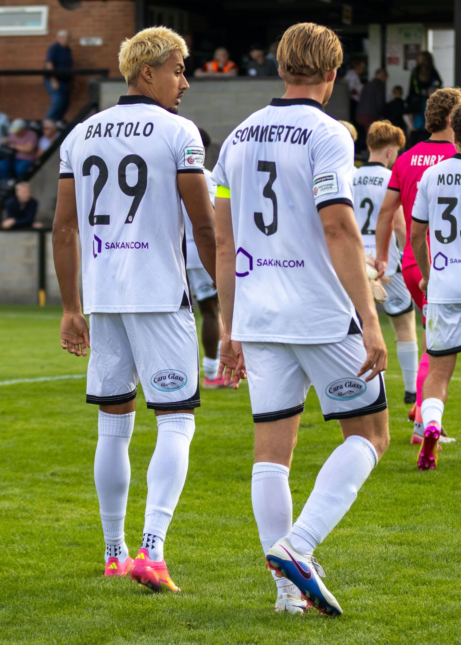 football players Bartolo #29 and Sommerton #3 in white uniforms walking on a football pitch after a match.