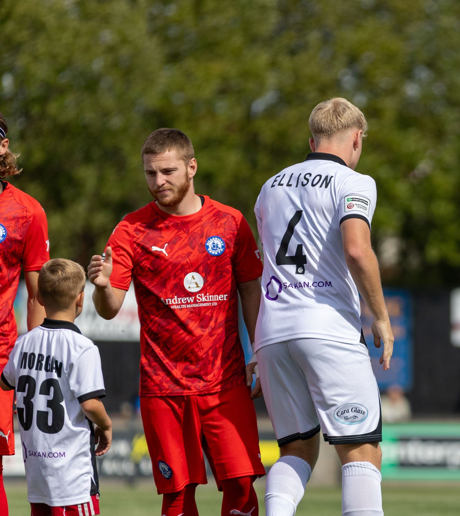 Soccer players shake hands on the field, with player Ellison wearing number 4 in a white kit during a match.