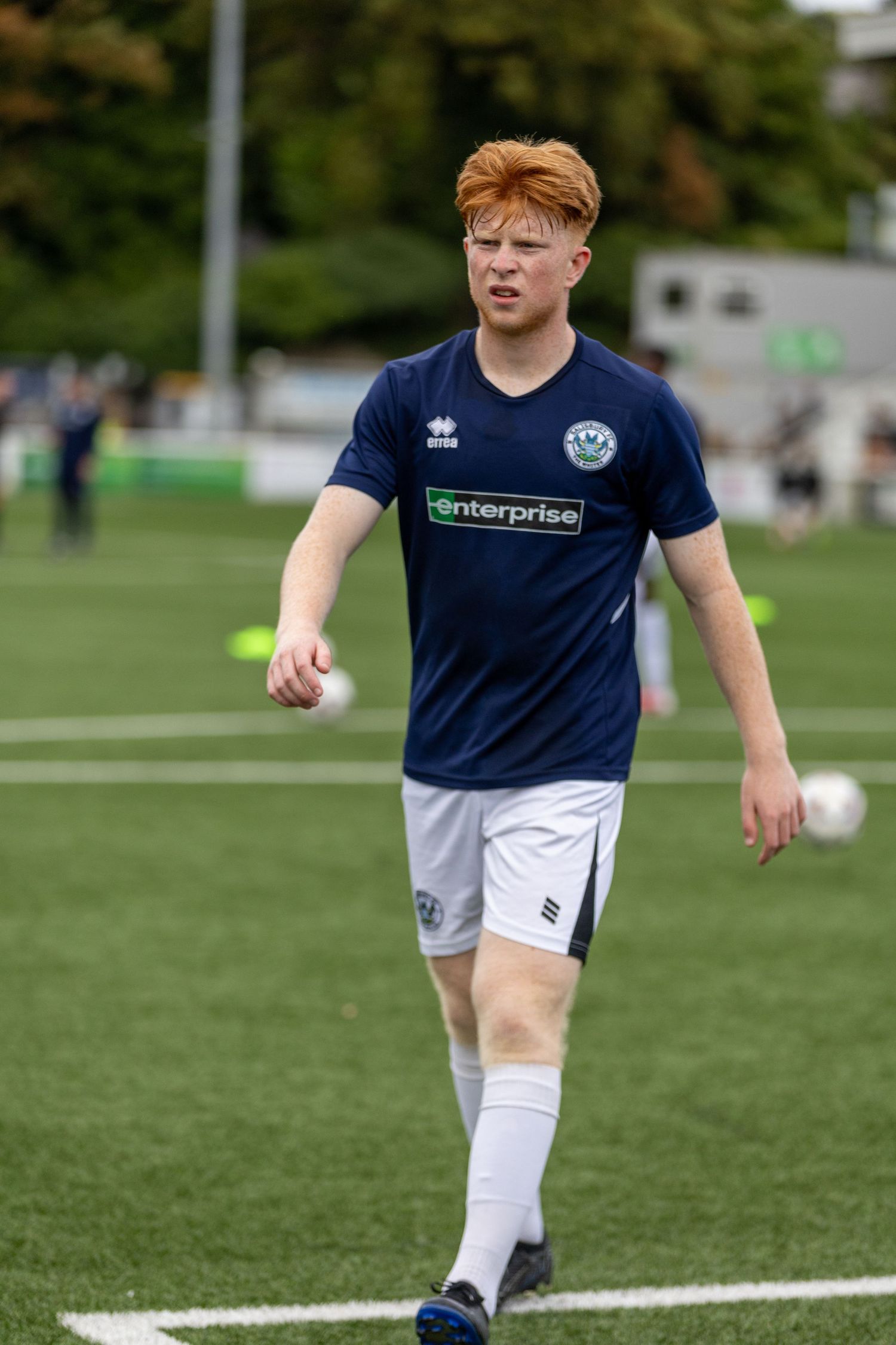 Young male soccer player in navy Enterprise jersey and white shorts walking on green turf during a match.
