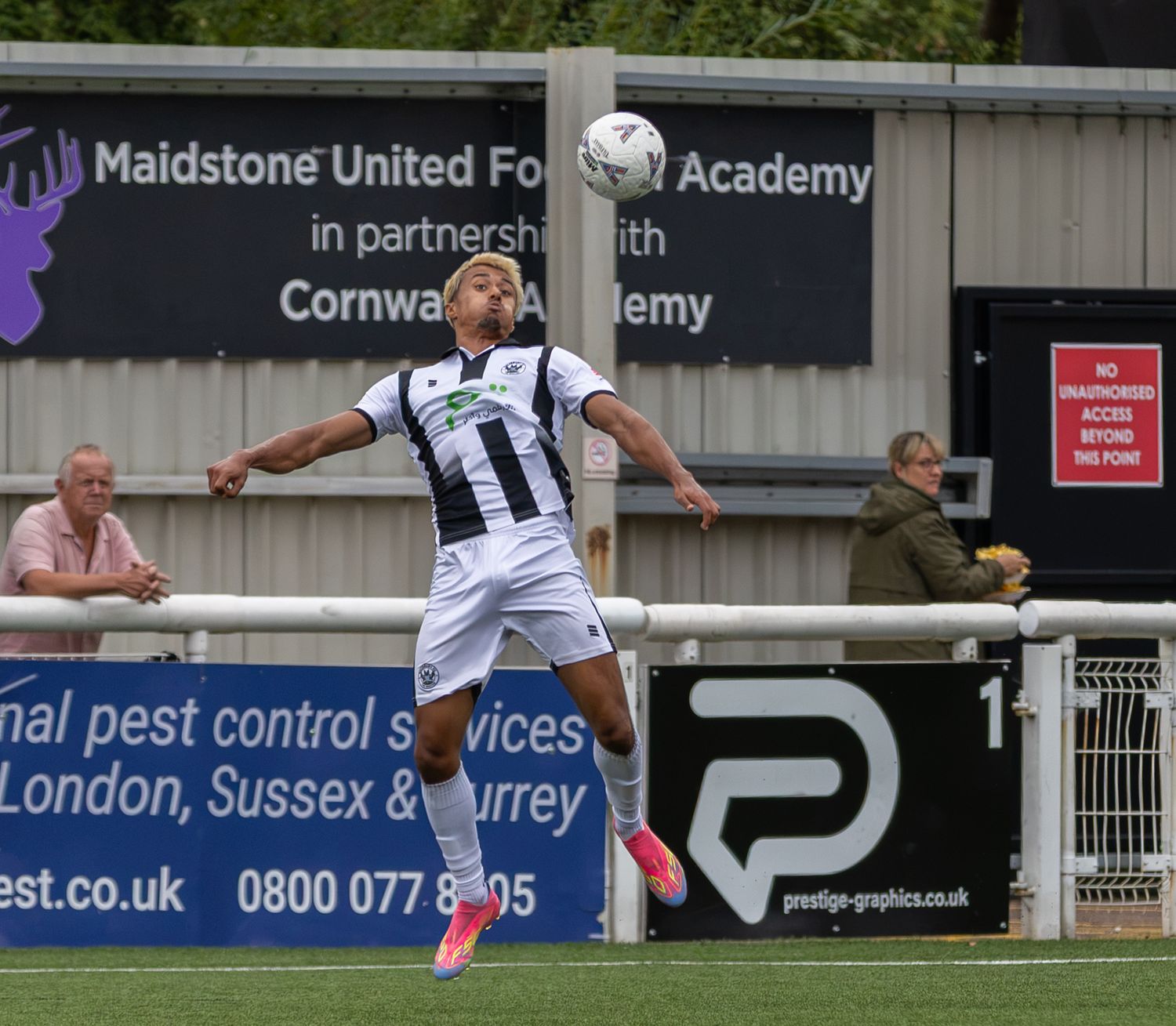 A footballer in black and white kit controls a ball mid-air at Maidstone United Football Academy.