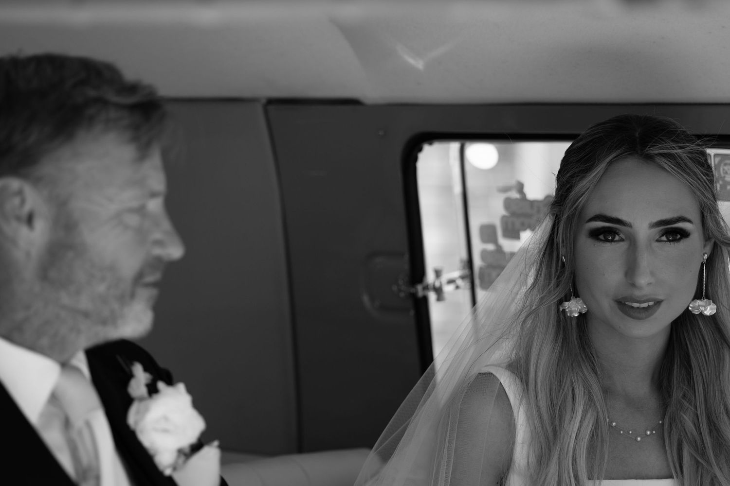 Black and white photo of a bride and her father sharing a tender moment inside a vintage wedding car.