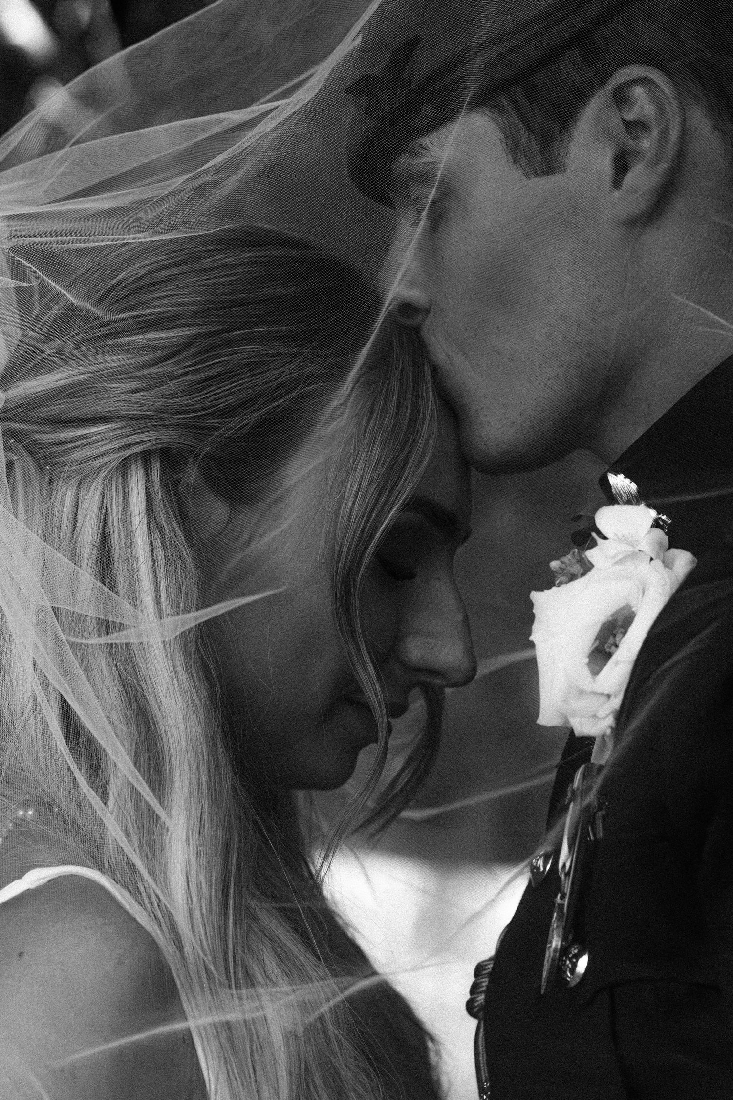 Black and white close-up of bride and groom in military uniform sharing an intimate moment under veil.