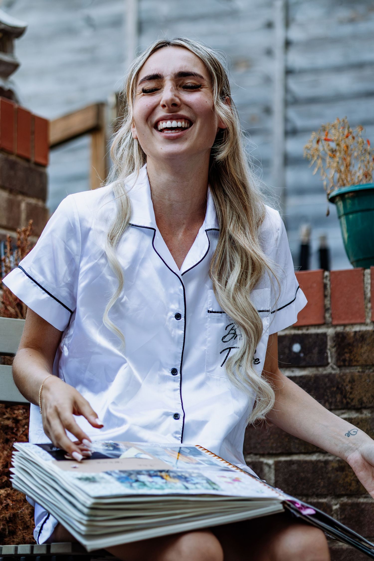 Laughing blonde bride in white pajamas enjoying photo album memories before wedding.