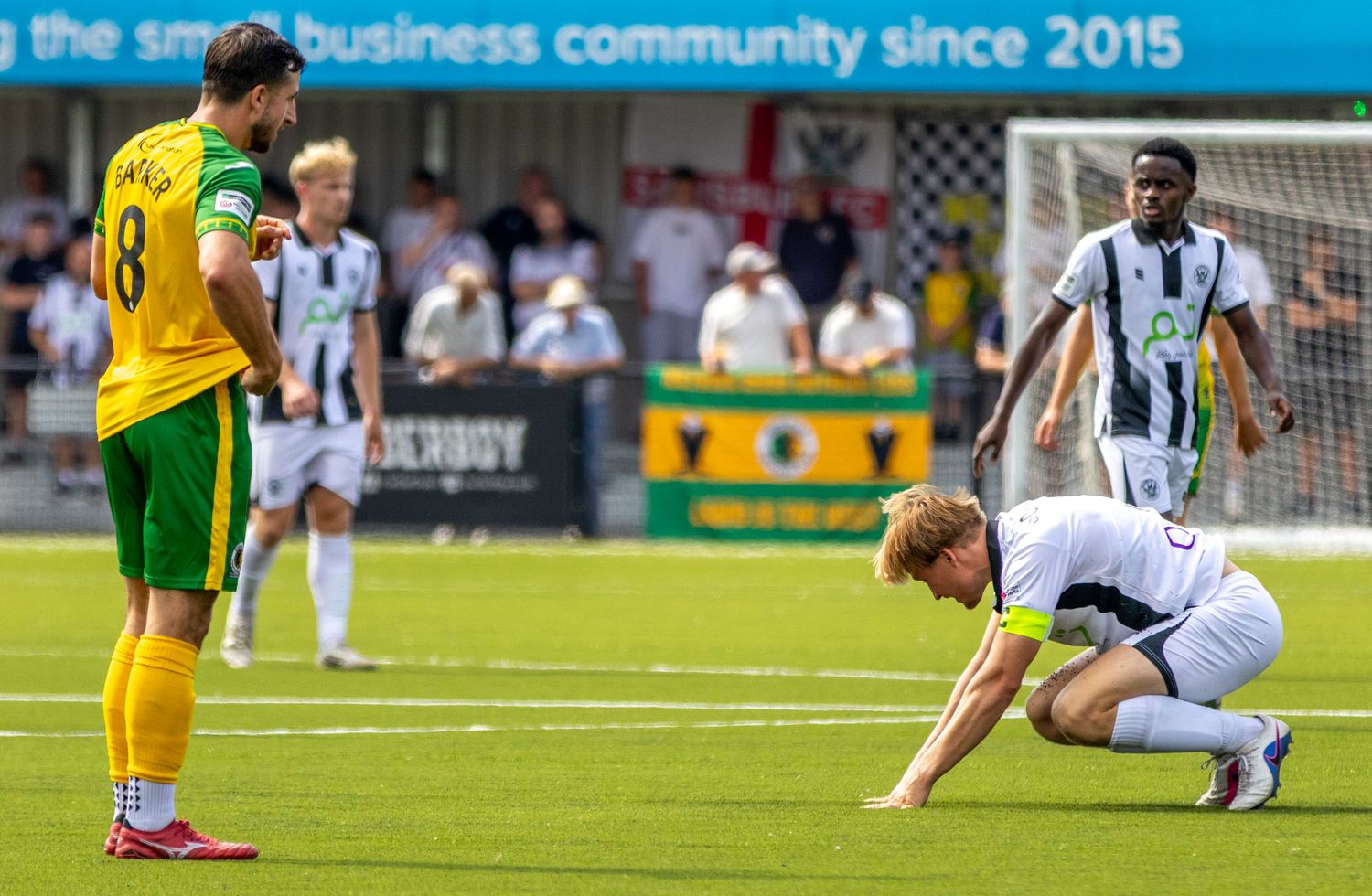 Football players in white and yellow-green kits pause during a competitive outdoor match.