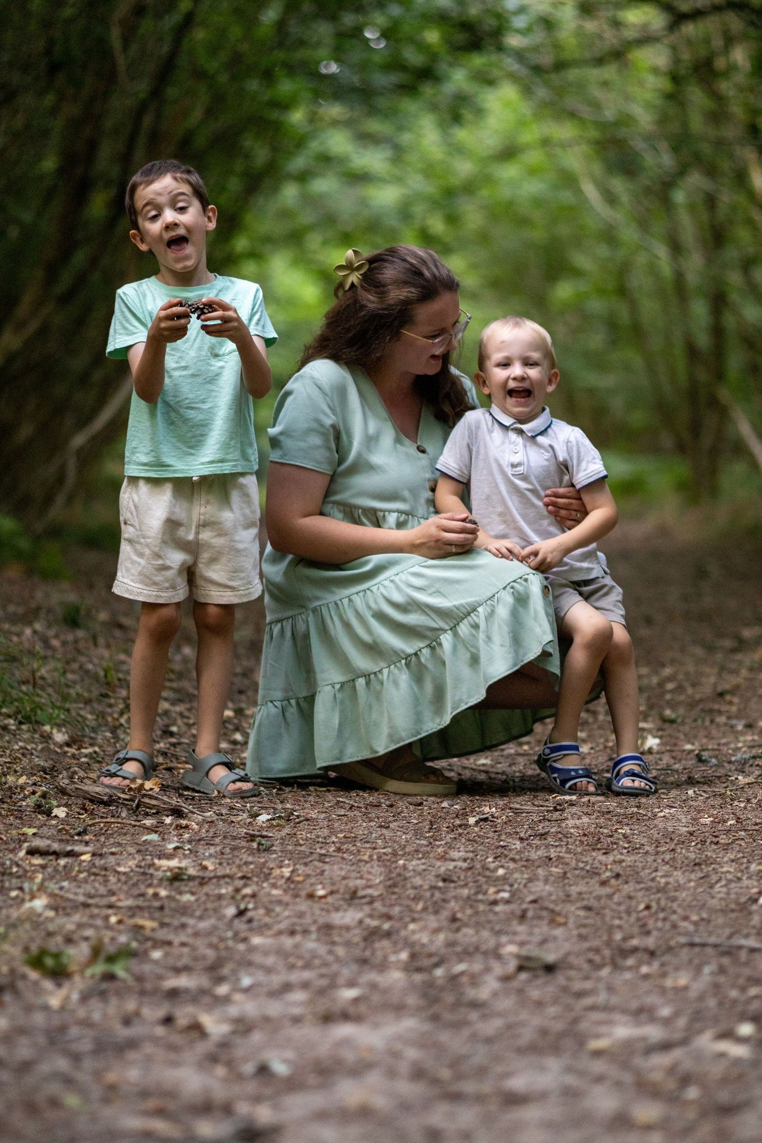 A laughing mother and her two energetic boys share a joyful moment on a woodland trail.
