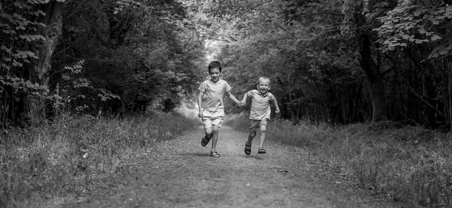 Black and white photo of two children running hand in hand along a forest path.